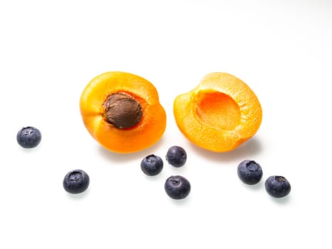A close up food photo of an apricot cut in half displayed with the pit and some ripe blueberries.