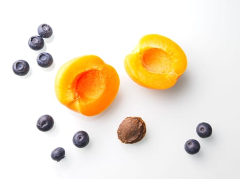 A close up flatlay food photo of an apricot cut in half displayed with the pit and some ripe blueberries.
