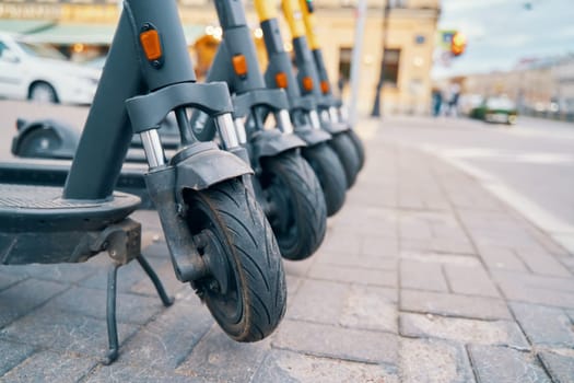 A line of motor vehicles with synthetic rubber tires and automotive design are parked on the sidewalk, their wheels rolling on the asphalt
