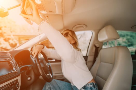 A woman in a white sweater adjusts the rearview mirror while sitting in the driver's seat of a car.