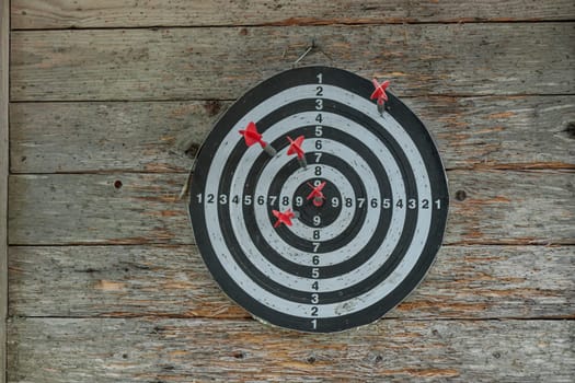 Closeup view of darts with a dart stuck into the board. Brick wall background. The dart stick is not in the center of the board