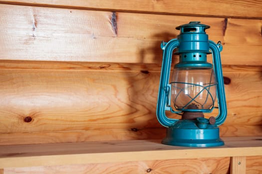The old vintage retro blue kerosene oil lamp on a wooden shelve inside the wooden countryside house background, banner