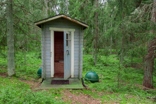 Wooden toilet in the forest. Blue colored natural bio WC cabin among trees on green grass. Finland
