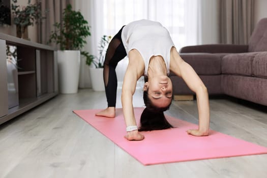 sporty woman doing yoga standing on the bridge on pink mat at home