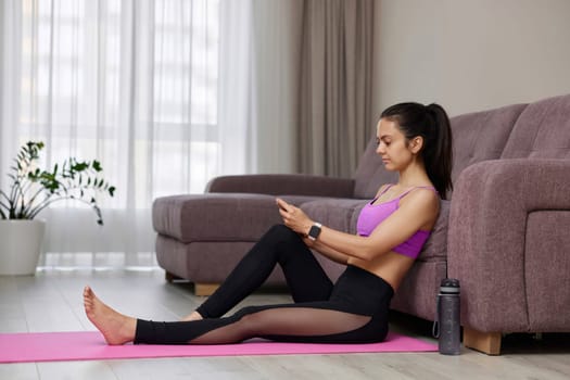 sporty woman sitting and using smartphone after her home workout at home