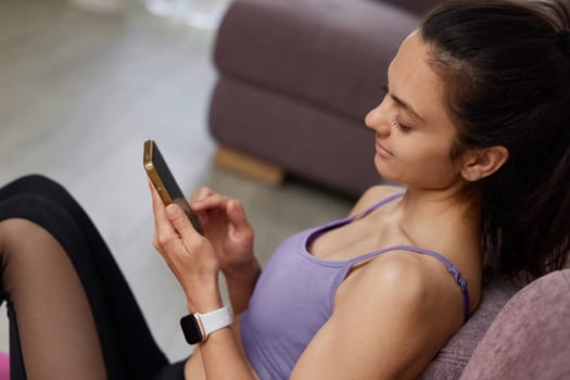 Caucasian sporty woman sitting and using smartphone at home