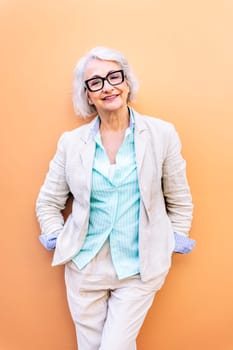 stylish mature entrepreneur woman smiling happy looking at camera leaning on an orange wall, concept of active lifestyle in adulthood, copyspace for text