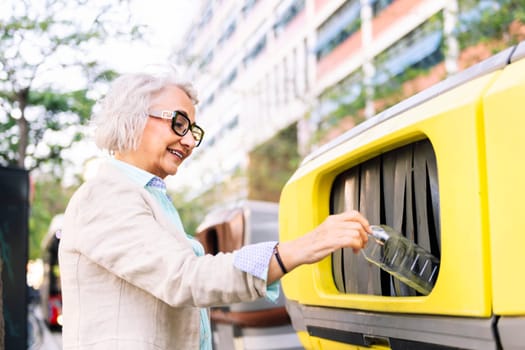 smiling mature woman throwing plastic into recycling bin, concept of sustainability and eco lifestyle
