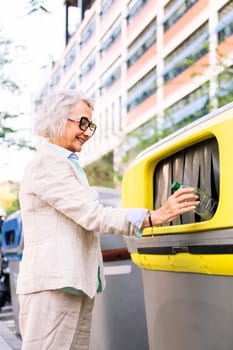 smiling mature woman throwing plastic into recycling bin, concept of sustainability and eco lifestyle