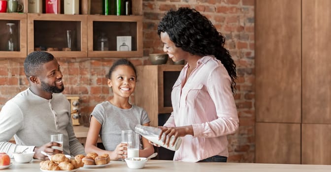 Little afro girl having breakfast with parents in kitchen, happy together, copy space