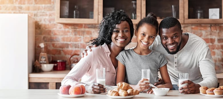 Beautiful black family having breakfast together, drinking milk and eating sweets at kitchen, copy space