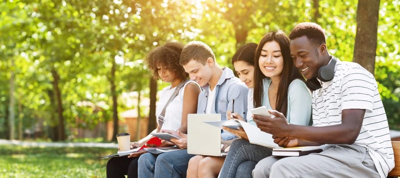 Education concept. Cheerful university students preparing for exam, talking and drinking coffee outdoors, sitting on bench in campus, free space