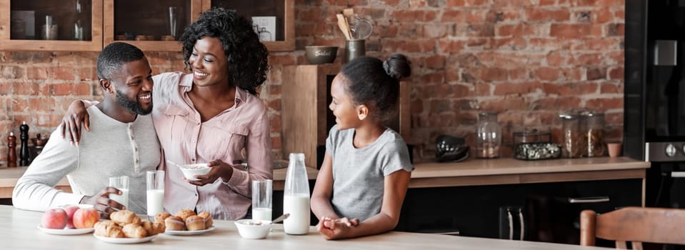 Joyful african father, mother and daughter having lunch together at home, talking and laughing, kitchen interior, free space