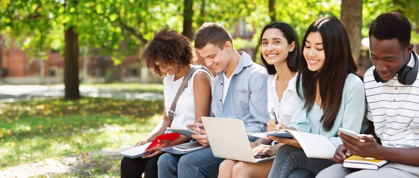 Group of international students preparing for classes together in university courtyard, smiling and enjoying summer weather