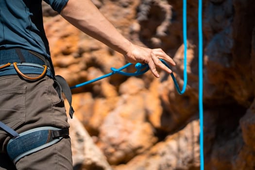 A young man prepares for rock climbing in the mountains outdoor, an athlete ties a figure eight loop on a rope during training, mountaineering on a sunny day, close-up view.