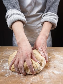 A close up photo of a woman's hands kneading a big ball of dough on a wooden cutting board.