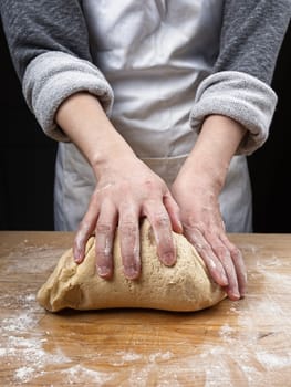 A close up photo of a woman's hands kneading a big ball of dough on a wooden cutting board.