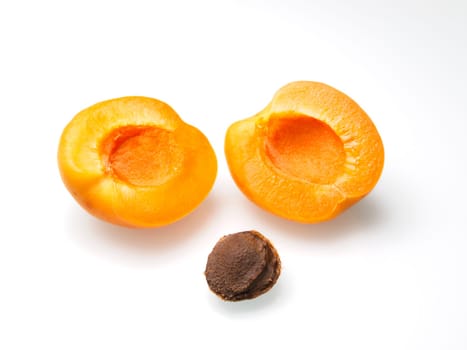 A close up food photo of an apricot cut in half with the pit on a white background.