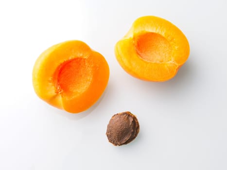 A close up food photo of an apricot cut in half with the pit on a white background.