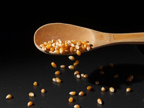 A conceptual  photo of yellow popcorn kernels falling off a wooden spoon onto a table. 