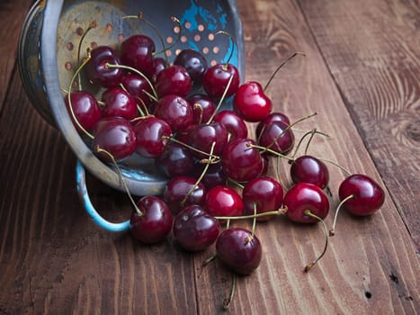 A close up display of cherries pouring out of an old collander on a wooden table.