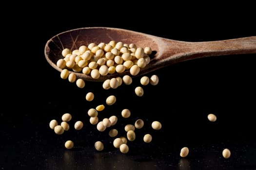 A concept photo of small dried soybeans falling off a spoon onto the table.