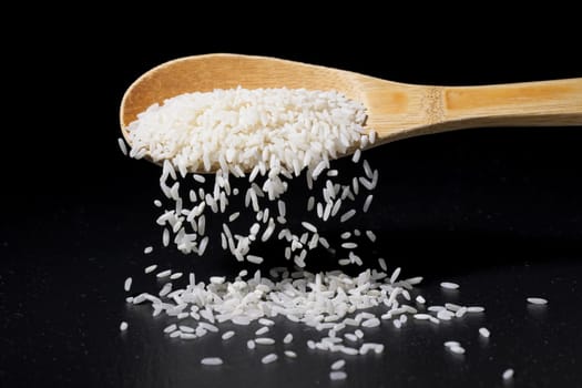 A conceptual photo of long grain white rice pouring off a wooden spoon and spilling onto the floor.