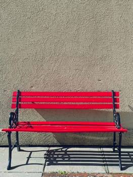 A bright red empty park bench sits against a solid wall on a sunny day in Cashmere, Washington.