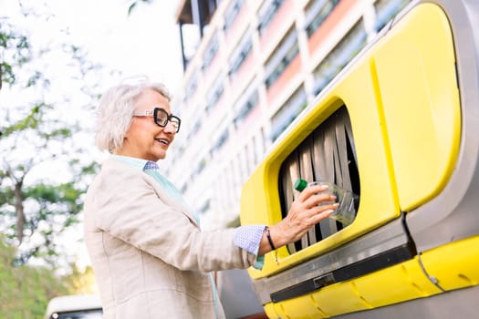 smiling mature woman throwing plastic into recycling bin, concept of sustainability and eco lifestyle