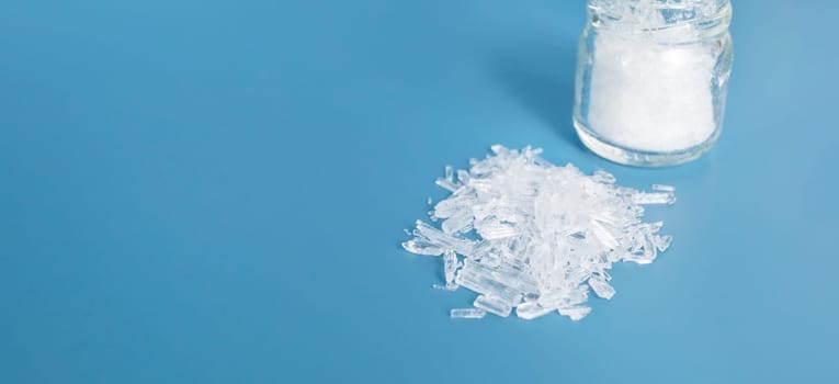 Banner Top View Organic Heap of Translucent Menthol Crystals on Blue Background, Glass Jar. Natural Ingredient for Producing Cosmetics. Horizontal Design Copy Space. High quality photo