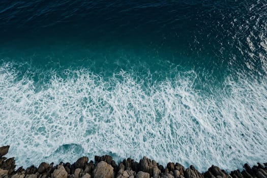 An aerial snapshot captures the dynamic interaction of deep blue waves with the intricate patterns of a rocky coast.