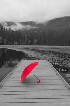 A concept black and white photo of a colored red umbrella resting on a dock at Sinclair Lake in north Idaho.