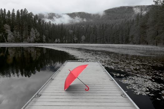 A concept black and white photo of a colored red umbrella resting on a dock at Sinclair Lake in north Idaho.