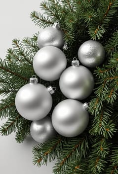 A close-up image of silver Christmas ornaments arranged within a cluster of evergreen branches. The ornaments are round and shiny, reflecting the light in a dazzling manner. The green branches provide a lush backdrop for the festive decorations.
