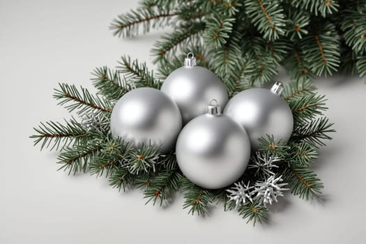 A close-up image of silver Christmas ornaments arranged within a cluster of evergreen branches. The ornaments are round and shiny, reflecting the light in a dazzling manner. The green branches provide a lush backdrop for the festive decorations.
