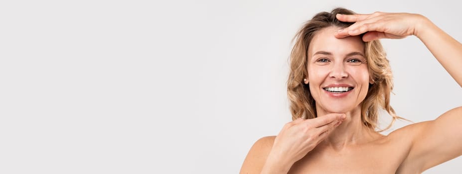 Facebuilding Concept. Happy Beautiful Middle Aged Woman Touching Chin And Forehead And Smiling At Camera, Attractive Mature Lady Massaging Face, Enjoying Anti-Aging Beauty Treatments, Copy Space