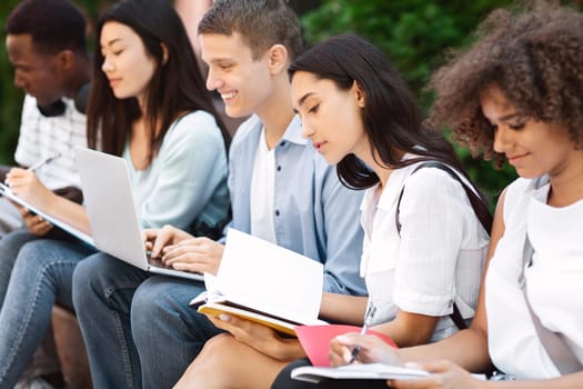 Multicultural group of students studying together outdoors, preparing for classes at campus
