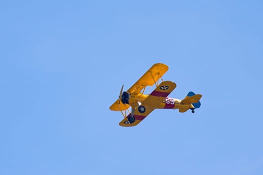 A yellow old style biplane soars up in the bright blue sky near Liberty Lake, Washington.