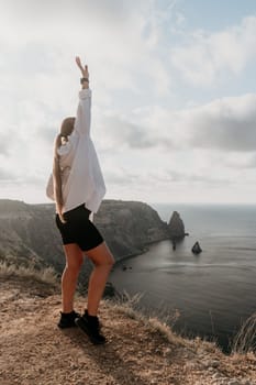 Woman travel sea. Young Happy woman in a long red dress posing on a beach near the sea on background of volcanic rocks, like in Iceland, sharing travel adventure journey