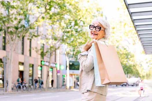 smiling mature woman standing with shopping bags at city, concept of happiness and urban lifestyle, copyspace for text