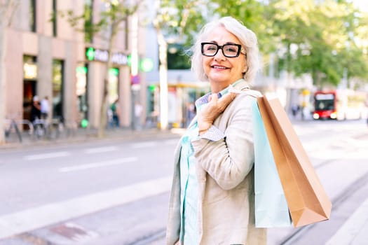 portrait of a smiling mature woman standing with shopping bags at city, concept of happiness and urban lifestyle, copyspace for text