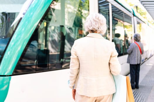 unrecognizable mature woman standing with shopping bags waiting for public transport, concept of sustainable mobility and urban lifestyle, copyspace for text