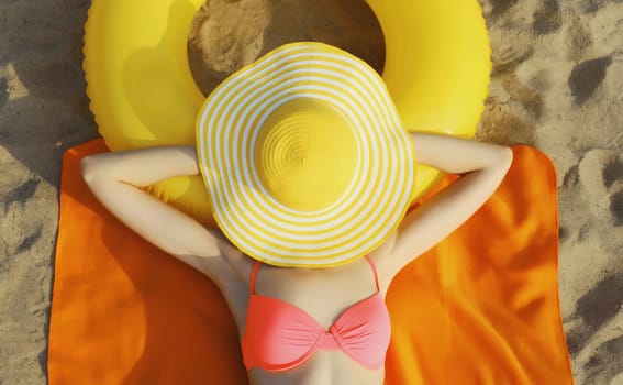 Summer vacation, happy relaxing young woman with straw hat covering her face lying on the sand on the beach with swimming inflatable ring