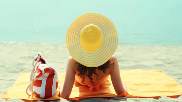 Summer vacation, beautiful happy relaxing young woman with yellow straw tourist hat lying on sand on the beach at sea