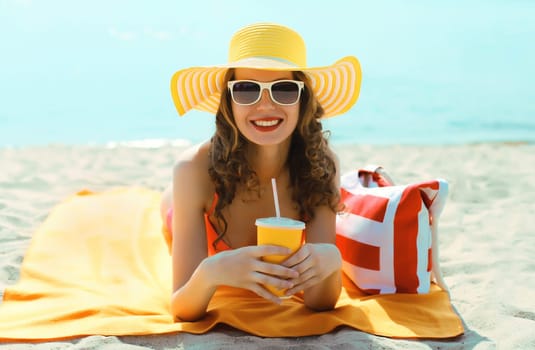 Summer vacation, tourism, happy relaxed woman smiles drinking juice with straw tourist hat lying on the sand on the beach against sea background