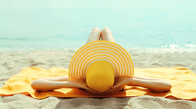 Summer vacation, beautiful happy relaxing young woman with yellow straw tourist hat lying on sand on the beach at sea