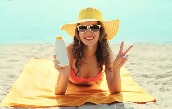 Summer vacation, happy smiling woman in tourist hat with suntan cream, lying on the sand on the beach against sea background