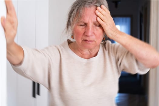 Unhappy mature woman touching head, feeling strong headache, at home alone, upset older female suffering from migraine or high blood pressure