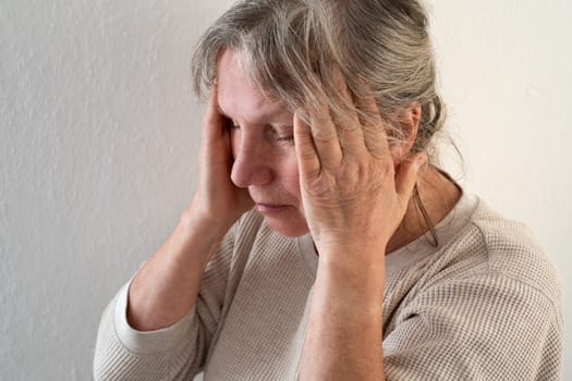Unhappy mature woman touching head, feeling strong headache, at home alone, upset older female suffering from migraine or high blood pressure