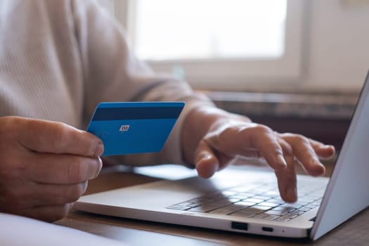 A cheerful mature woman is making an online purchase or payment, utilizing a credit card and a laptop computer. Online banking concept.